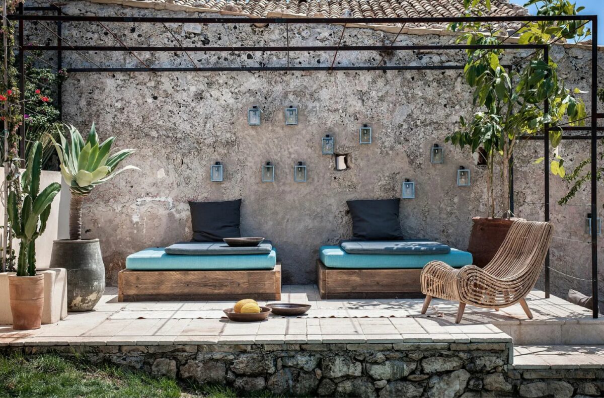 Outdoor seating surrounded by outdoor plants against the wall of a stone villa