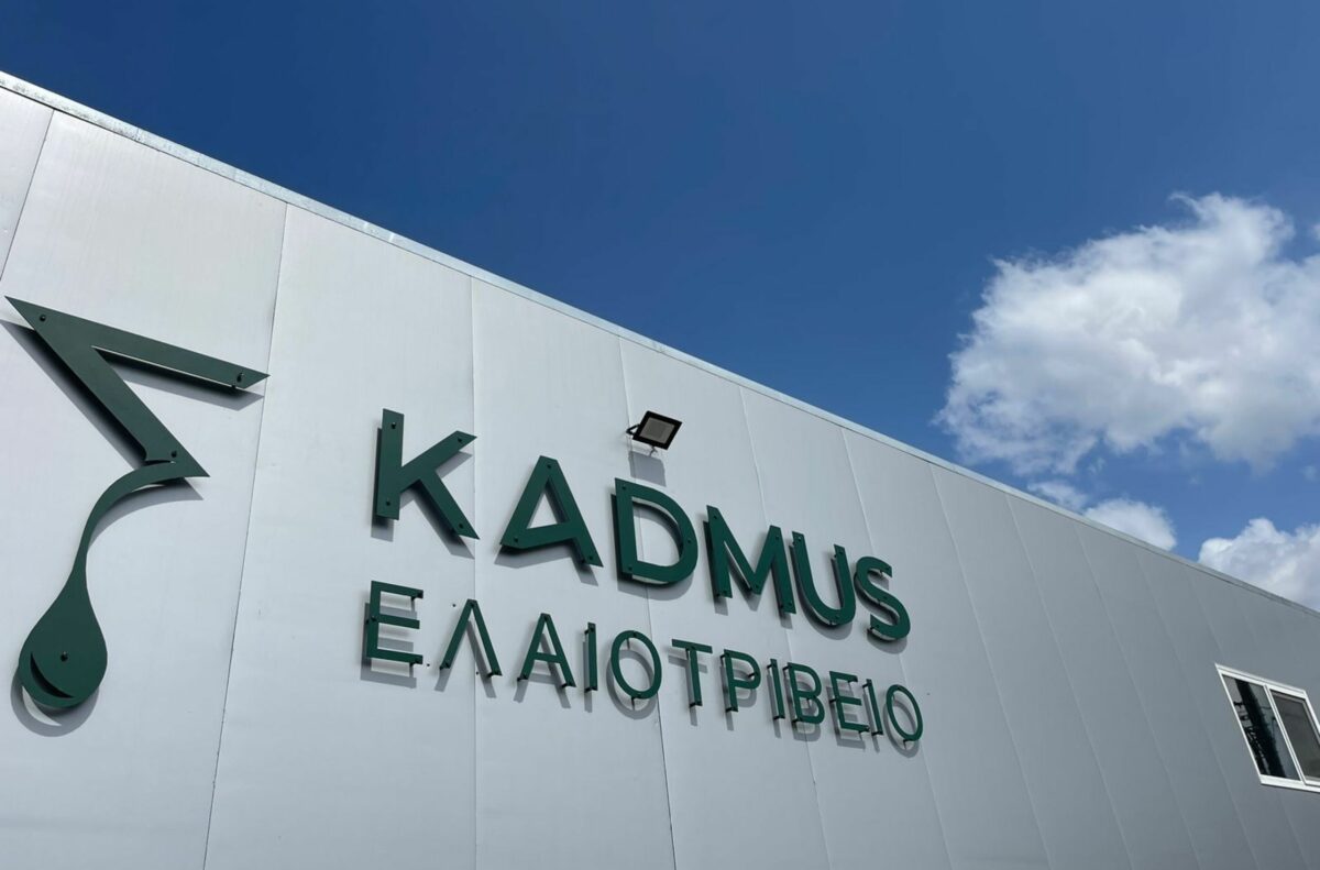 Εξωτερικό του ελαιοτριβείο Kadmus με το λογότυπο και την πινακίδα της με ηλιόλουστο φόντο